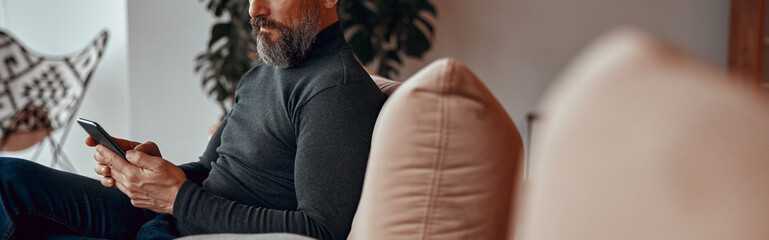 Side view of man sitting in comfortable armchair while typing on his phone in office space