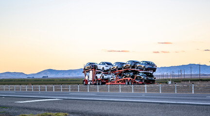 Classic big rig car hauler semi truck transporting cars on the red modular semi trailer driving on...