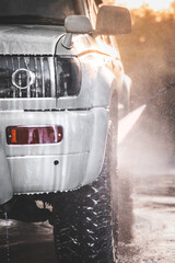 Washing white car at a self-service car wash with a high-pressure water jet after off-road driving,...