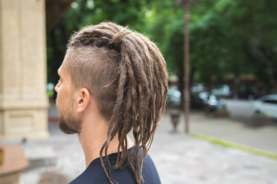 Back view of a caucasian man with dreadlocks and sidecut on a summer street.