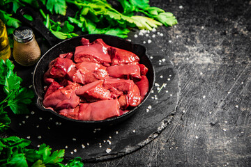 Pieces of raw liver in a frying pan with parsley and spices. 