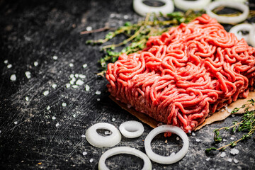 A piece of fresh minced meat on paper with onion rings and thyme. 