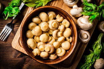 Pickled mushrooms in a bowl on a cutting board with greens. 