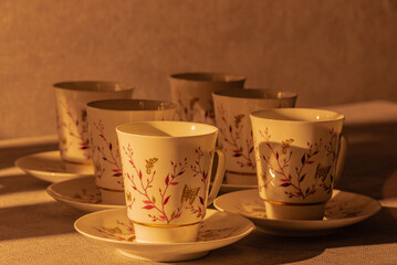 Clean empty Cups and saucers, standing in a row on the table, illuminated by the setting sun.
