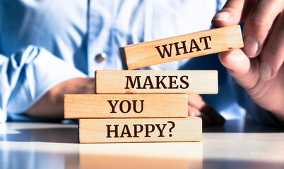 Close up on businessman holding a wooden block with "What Makes You Happy?" message