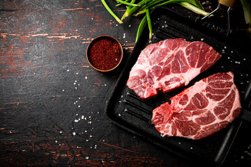 Raw pork steak in a frying pan with green onions and spices. 