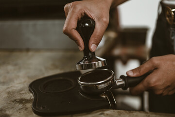 Barista using a tamper to press ground coffee into a portafilter. Coffee maker concept..