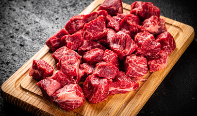 Raw pieces of beef on a wooden cutting board.