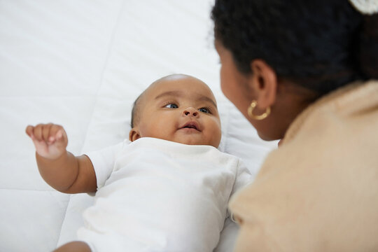 African adorable baby looking mother on bed