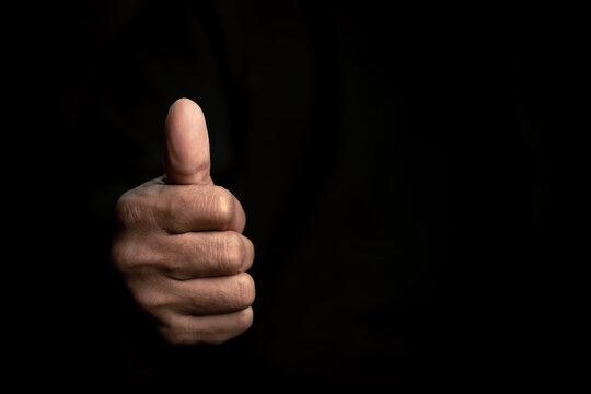 The symbol is "super ok". Young man's hand on a black background isolated close-up thumbs up to show approval and a positive sign.
