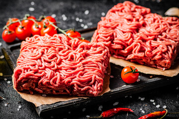 Raw minced meat on a cutting board with cherry tomatoes. 