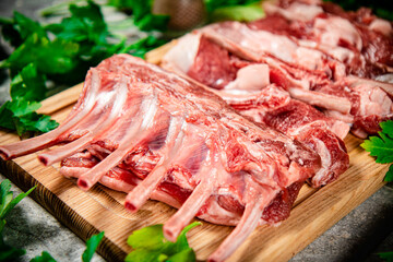 Raw rack of lamb on a wooden cutting board with parsley. 