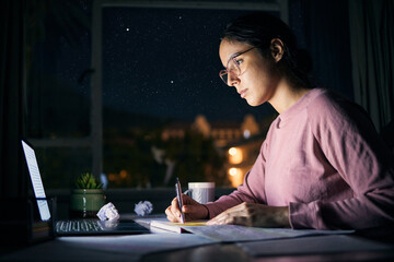 Girl, reading and studying on laptop at night for research, education and internet project. Serious young student, writing notes and learning on computer at dark desk for homework, planning and tech