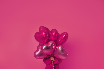A girl holds pink balloons in front of her on a pink background in a pink dress. Young woman on birthday holiday party. Valentine's Day, February 14.
