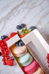 Macaron dessert, a box with colorful macarons lies on a marble style. Sweets, diet, gift for March 8 or February 14. Strawberries and lingonberries, blueberries.