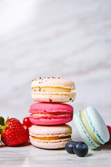 Macaron pink, orange and beige, blue on marble style. A beautiful and beautiful French dessert. Fruits, Strawberries and lingonberries, blueberries, raspberries.