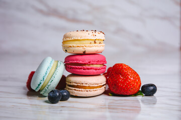 Macaron pink, orange and beige, blue on marble style. A beautiful and beautiful French dessert. Fruits, Strawberries and lingonberries, blueberries, raspberries.