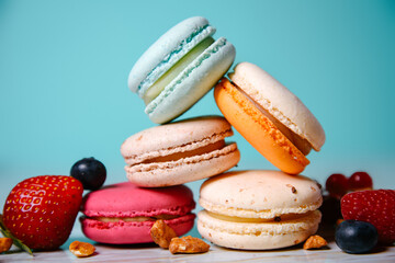 Colorful macarons. Small French cakes. Sweet and colorful french macaroons. Many tasty macarons with fresh berries, raspberries and blueberries, nuts and strawberries on a green background