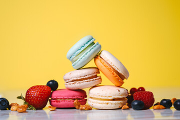 Colorful macarons. Small French cakes. Sweet and colorful french macaroons. Many tasty macarons with fresh berries, raspberries and blueberries, nuts and strawberries on a yellow background.