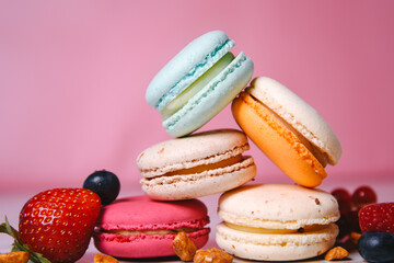 Colorful macarons. Small French cakes. Sweet and colorful french macaroons. Many tasty macarons with fresh berries, raspberries and blueberries, nuts and strawberries on a pink background.