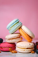 Colorful macarons. Small French cakes. Sweet and colorful french macaroons. Many tasty macarons with fresh berries, raspberries and blueberries, nuts and strawberries on a pink background.