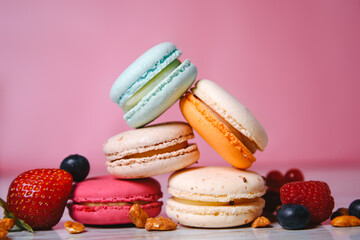 Colorful macarons. Small French cakes. Sweet and colorful french macaroons. Many tasty macarons with fresh berries, raspberries and blueberries, nuts and strawberries on a pink background.