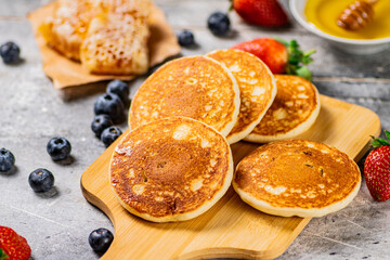 Homemade pancakes on a cutting board with honey and berries. 