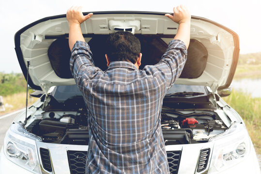 A young man having trouble with his broken car looks frustrated at the engine failure.