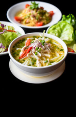 Chicken soup Pho ga  in vietnamese style on black background with banh mi bread, salad and pasta carbonara