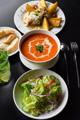 Lunch set made of tomato cream soup, salad, chicken with potato, lemonade on black background
