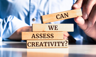 Close up on businessman holding a wooden block with "Can We Assess Creativity?" message