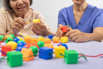 Caregiver and senior woman playing stringing beads game for dementia prevention