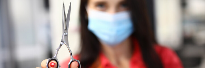 Woman hairdresser in protective mask holds scissors