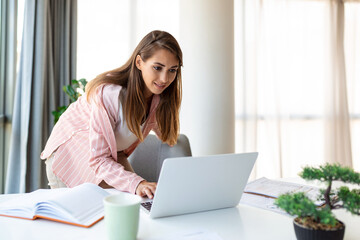 Fototapeta premium Beautiful smiling businesswoman reading something on a laptop while leaning on the table in the office