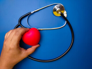 Hand holding red heart with statehoscop on blue background. Healthcare and medical concept.