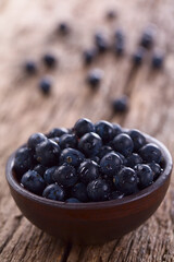 Fresh raw Patagonian Calafate berries (lat. Berberis heterophylla) in rustic bowl, photographed on wood (Selective Focus, Focus one third into the image)
