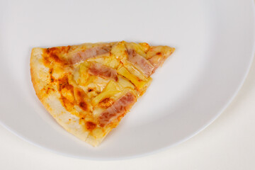 Closeup studio shot of one piece of tasty delicious Italian homemade mozzarella cheesy ham and pineapple original Hawaiian pizza soft bread crust on white dish plate served on table in restaurant