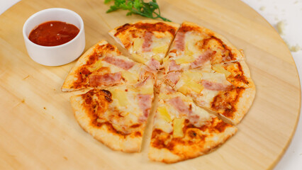 Closeup top view studio shot of tasty delicious Italian homemade mozzarella cheesy ham pineapple original Hawaiian pizza soft bread crust on wodden plate served on table with ketchup in restaurant