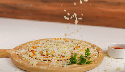 Closeup studio shot of hot oven baked tasty delicious Italian homemade ham pineapple original soft bread crust pizza on wooden plate pan while sprinkling mozzarella cheese on top with tomato ketchup