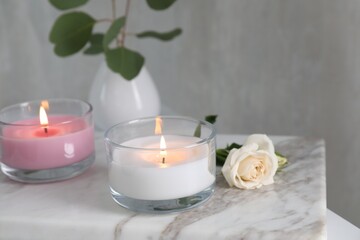 Fototapeta na wymiar Burning candles and beautiful rose on white marble board