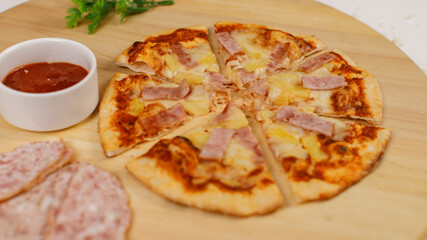 Closeup top view studio shot of tasty delicious Italian homemade mozzarella cheesy ham pineapple original Hawaiian pizza soft bread crust on wodden plate served on table with ketchup in restaurant