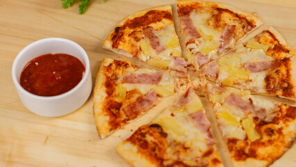 Closeup top view studio shot of tasty delicious Italian homemade mozzarella cheesy ham pineapple original Hawaiian pizza soft bread crust on wodden plate served on table with ketchup in restaurant
