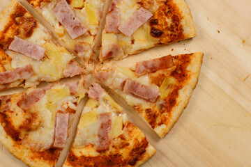 Closeup top view studio shot of tasty delicious Italian homemade mozzarella cheesy ham pineapple original Hawaiian pizza soft bread crust on wodden plate served on table in restaurant.