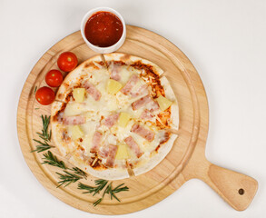 Closeup top view studio shot of round hot oven baked tasty delicious Italian homemade ham pineapple original Hawaiian soft bread crust pizza on wooden plate pan with tomatoes and ketchup on table