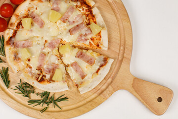 Closeup top view studio shot of round hot oven baked tasty delicious Italian homemade ham pineapple original Hawaiian soft bread crust pizza on wooden plate pan with tomatoes and ketchup on table