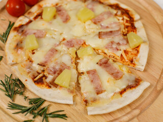 Closeup top view studio shot of round hot oven baked tasty delicious Italian homemade ham pineapple original Hawaiian soft bread crust pizza on wooden plate pan with tomatoes and ketchup on table