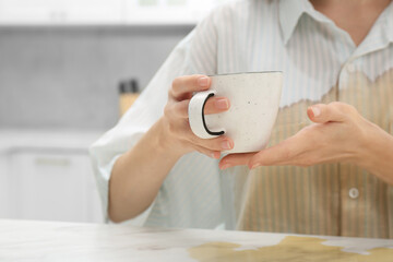 Woman with spilled coffee over her shirt at marble table in kitchen, closeup. Space for text