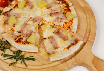 Closeup top view studio shot of round hot oven baked tasty delicious Italian homemade ham pineapple original Hawaiian soft bread crust pizza on wooden plate pan with tomatoes and ketchup on table