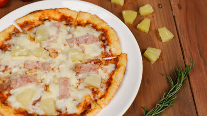 Closeup top view studio shot of round hot oven baked tasty delicious Italian homemade ham pineapple original Hawaiian soft bread crust pizza on wooden plate pan with tomatoes and ketchup on table