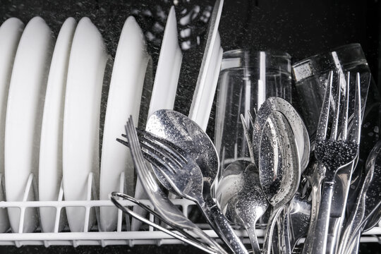 Clean wet plates and cutlery in dishwasher, closeup